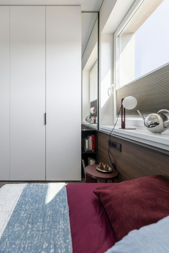 Narrow bedroom with a tall white wardrobe along one wall and a bed by the window